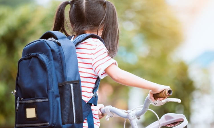 маленькая девочка на велосипеде с синим рюкзаком для школы