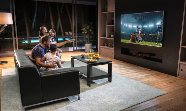семья сидит перед большим телевизором и смотрит футбол