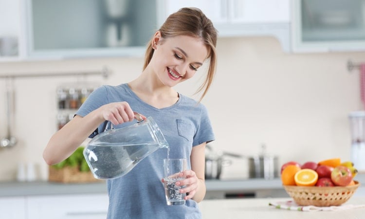женщина наливает чистую воду из кувшина в стакан