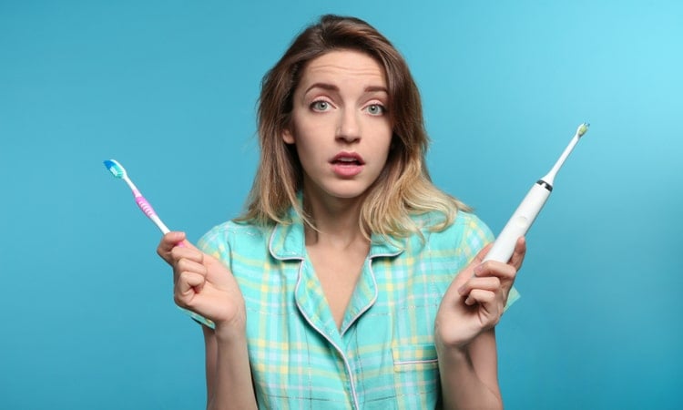 sieviete izvelas starp parasto un elektrisko zobu birsti
