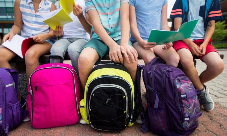дети сидят на скамейке и держат разноцветные рюкзаки для школы