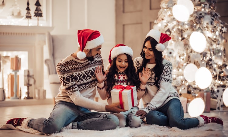 родители в одинаковых свитерах дарят ребенку рождественский подарок