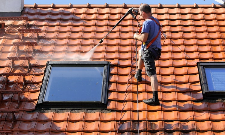 мужчина моет крышу с помощью мойки высокого давления